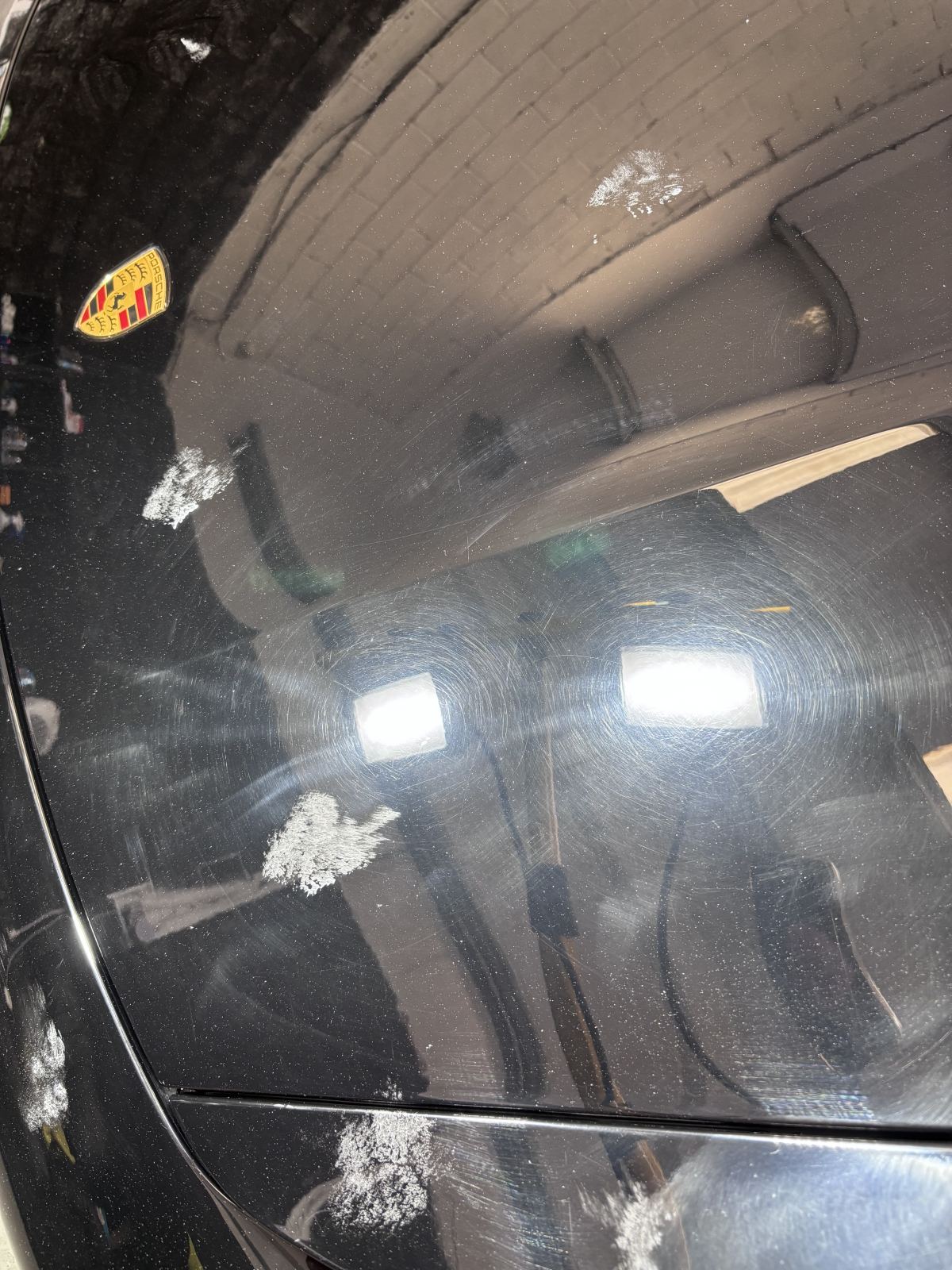 Porsche paintwork before correction showing swirl marks under detailing lights