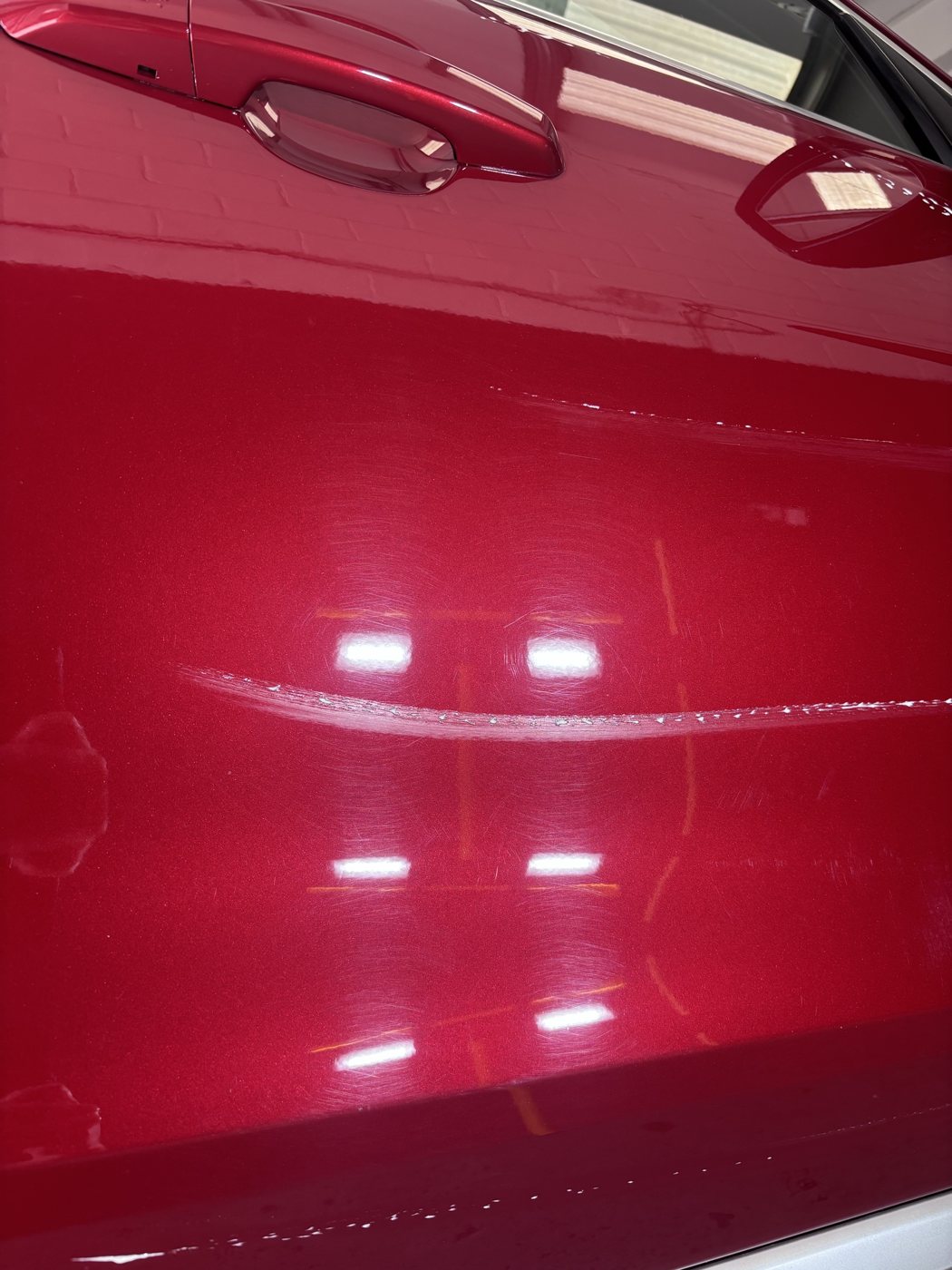 Deep scratches and swirl marks on a red door under the inspection lights before paint correction
