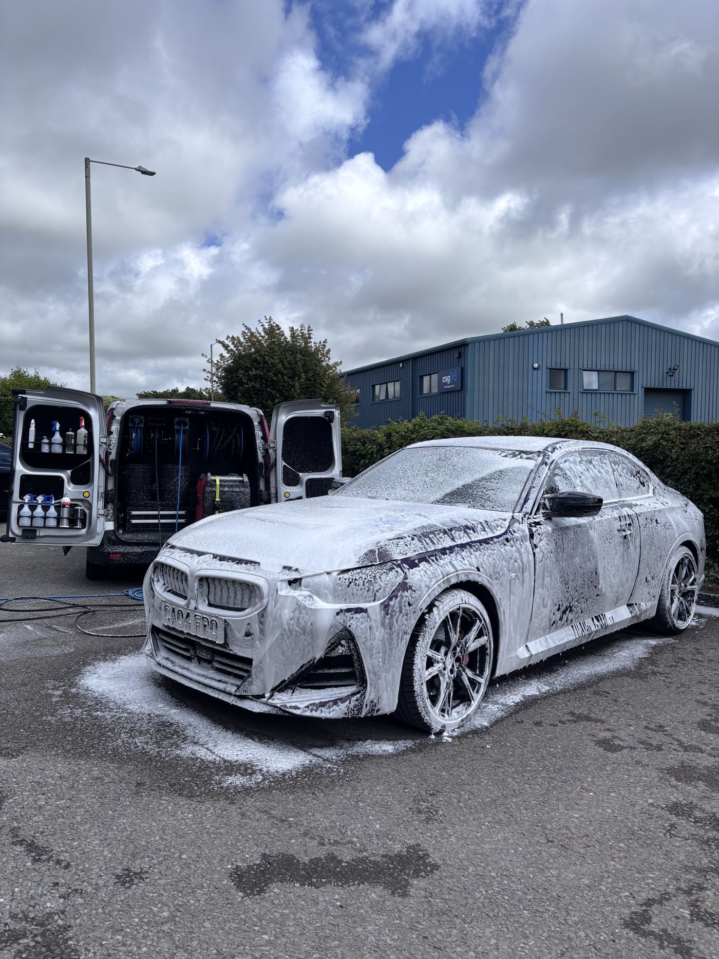 BMW covered in pre-wash snow foam beside the detailing van